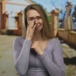 A woman with a sad expression is wiping her tears in an outdoor setting
