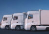 Three white trucks parked side by side in an urban area at dusk