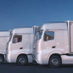 Three white trucks parked side by side in an urban area at dusk