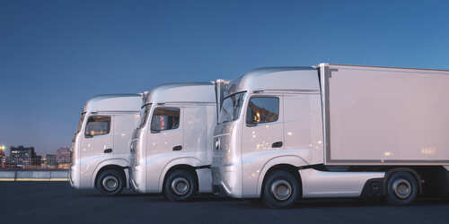 Three white trucks parked side by side in an urban area at dusk