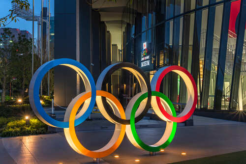 shutterstock_1970735831.jpg Illuminated Olympic rings displayed outside a modern building at night