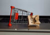 A miniature shopping cart next to a crumpled paper bag with a shopping cart icon