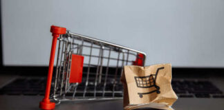 A miniature shopping cart next to a crumpled paper bag with a shopping cart icon
