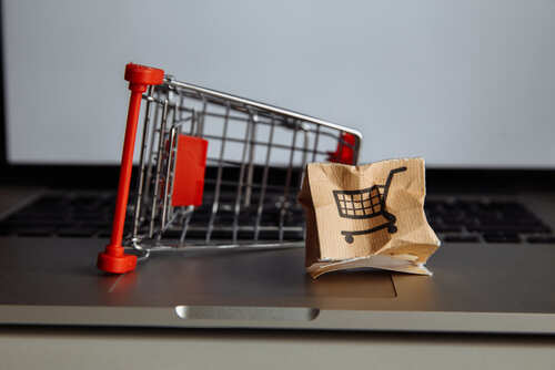 shutterstock_1845999724.jpg A miniature shopping cart next to a crumpled paper bag with a shopping cart icon