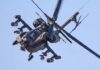 An Apache helicopter flying in the sky with visible rotor blades