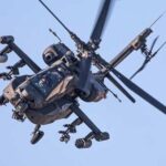 An Apache helicopter flying in the sky with visible rotor blades