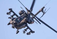 An Apache helicopter flying in the sky with visible rotor blades