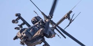 An Apache helicopter flying in the sky with visible rotor blades