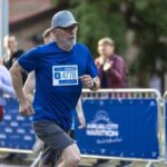 An older man running in a marathon wearing a blue shirt and a race bib