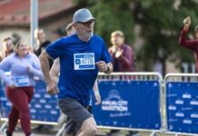 An older man running in a marathon wearing a blue shirt and a race bib