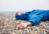 A person in a blue jacket lying on a pebbled beach with a blurred background