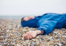 A person in a blue jacket lying on a pebbled beach with a blurred background