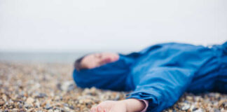 A person in a blue jacket lying on a pebbled beach with a blurred background