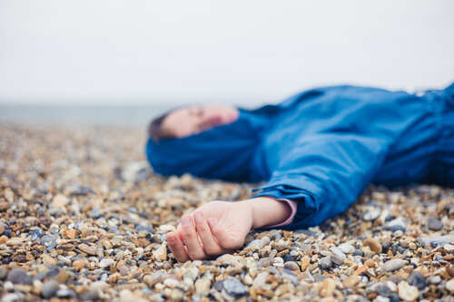 A person in a blue jacket lying on a pebbled beach with a blurred background