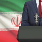 A suited individual standing behind a podium with microphones in front of the Iranian flag
