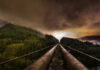 Panoramic view of industrial pipes leading towards a mountainous landscape under a cloudy night sky