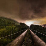 Panoramic view of industrial pipes leading towards a mountainous landscape under a cloudy night sky