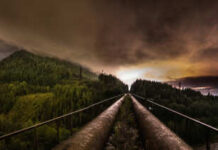 Panoramic view of industrial pipes leading towards a mountainous landscape under a cloudy night sky