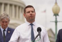 A politician speaking at a press conference outdoors with colleagues in the background