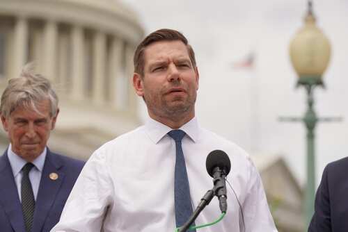 A politician speaking at a press conference outdoors with colleagues in the background