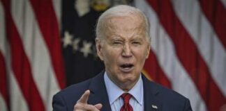 A man in a suit delivering a speech in front of American flags