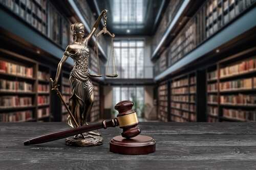 A statue of Lady Justice holding scales next to a gavel in a law library