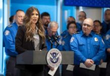 A woman speaking at a podium with law enforcement officers in the background