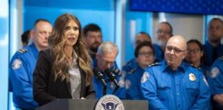 A woman speaking at a podium with law enforcement officers in the background