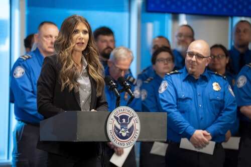 A woman speaking at a podium with law enforcement officers in the background