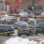 Multiple police vehicles at a scene with caution tape and emergency lights activated