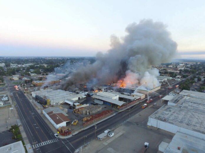 A large industrial fire with thick smoke rising into the sky and firefighters responding