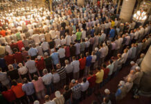 A large group of men participating in a prayer service inside a mosque