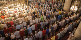 A large group of men participating in a prayer service inside a mosque